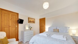 A bedroom with a bed, a dresser, a TV mounted on the wall, and a wooden door.