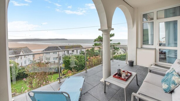 A balcony with a view of the sea, a lounge chair, a sofa, and a table with a tray. - 3 Bed in Woolacombe (oc-n1711) (Woolacombe)