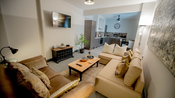 A modern living room with a sofa set, a coffee table, and a TV mounted on the wall. - Lovely House with parking, garden, dogs welcome. Sleeps up to 7. Central Wirral (Heswall)