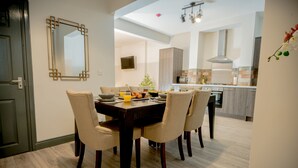 A dining area with a dark wooden table and beige chairs, a kitchen in the background, and a mirror on the wall. - Lovely House with parking, garden, dogs welcome. Sleeps up to 7. Central Wirral (Heswall)