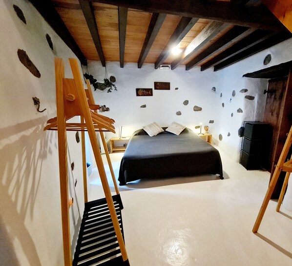 A bedroom with a bed, wooden beams, a dresser, and a wall decorated with rocks and shells.