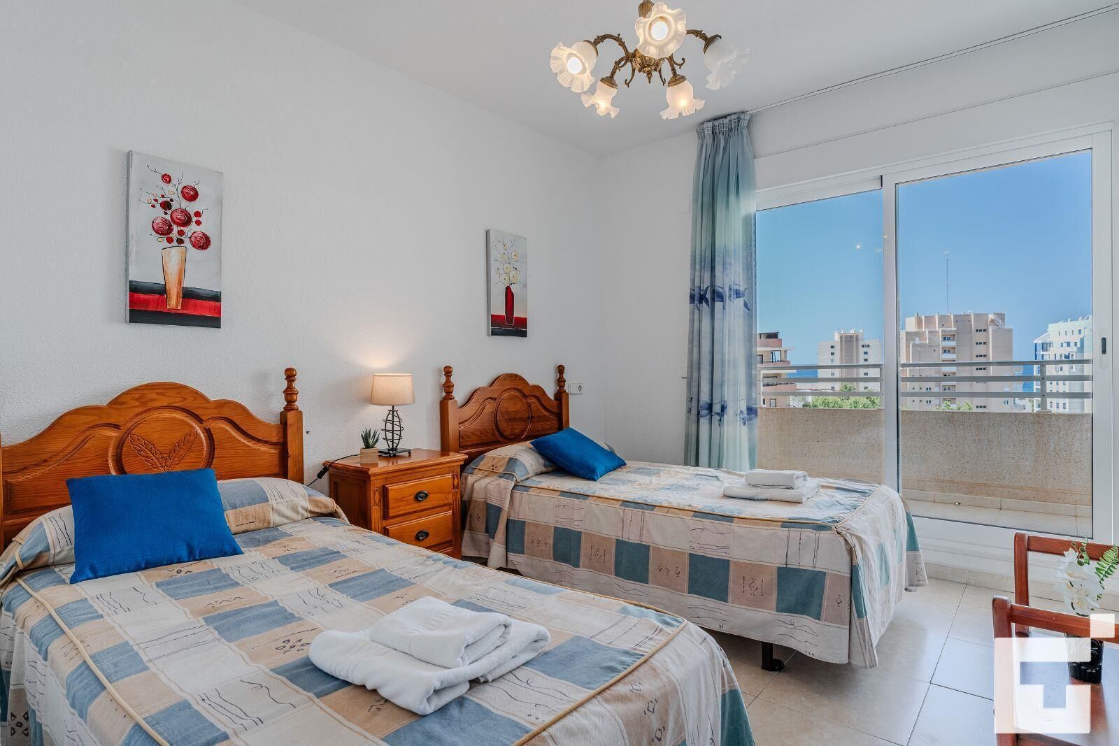 Une chambre d’hôtel avec deux lits, une table de chevet, une lampe et une vue sur la ville grâce à de grandes fenêtres.