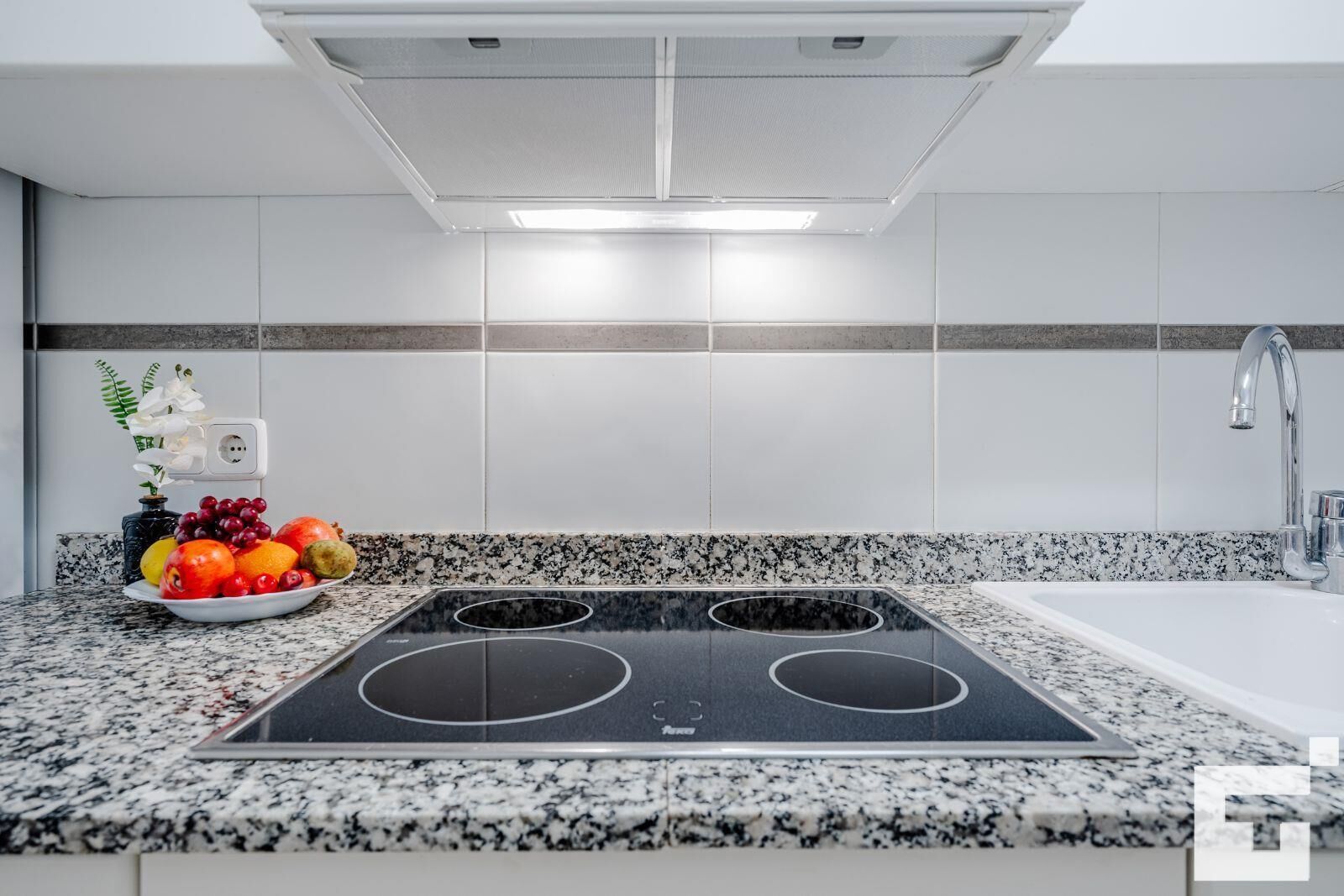 A modern kitchen with a black induction cooktop, a white sink, and a granite countertop.
