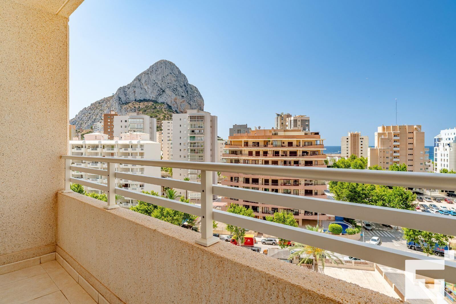 A balcony with a view of a mountain and cityscape, including buildings and parked cars.