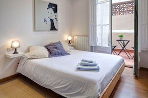 A bedroom with a bed, two bedside lamps, a wall-mounted artwork, and a view of an outdoor patio.