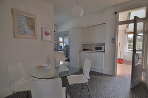 A compact kitchen with white cabinets, a microwave, and a glass dining table with chairs.