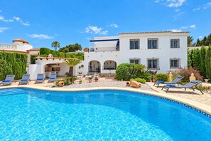 A poolside area with a clear blue pool, lounge chairs, and a white building with multiple windows and balconies. - Large and comfortable villa  with private pool in Javea, on the Costa Blanca, Spain for 8 persons (Javea)