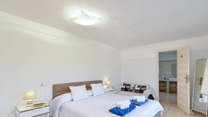 A hotel room with a large bed, bedside tables with lamps, a bathroom visible through an open door, and a tiled floor. - Large and comfortable villa  with private pool in Javea, on the Costa Blanca, Spain for 8 persons (Javea)