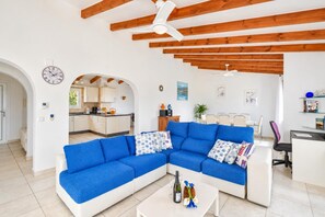 A modern living room with a blue sectional sofa, a white coffee table with a bottle and glasses, and a kitchen visible through an archway. - Large and comfortable villa  with private pool in Javea, on the Costa Blanca, Spain for 8 persons (Javea)