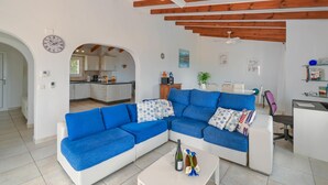 A modern living room with a blue sectional sofa, a white coffee table with drinks, and a kitchen in the background. - Large and comfortable villa  with private pool in Javea, on the Costa Blanca, Spain for 8 persons (Javea)