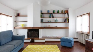 Uma sala de estar com lareira, estantes de livros, um sofá e um banquinho.