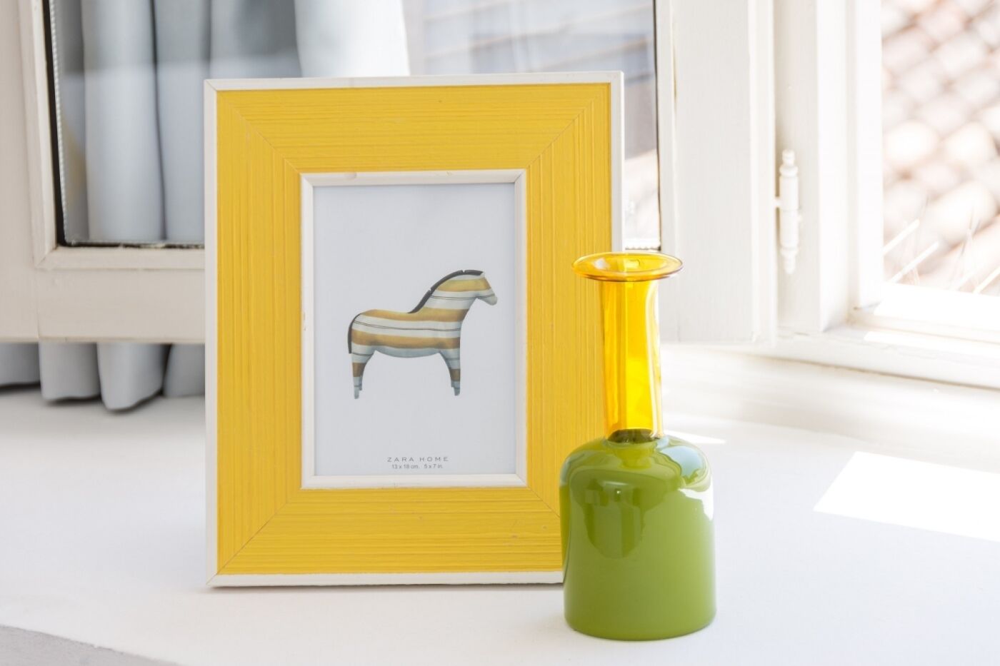 A framed artwork of a striped horse on a white surface next to a green bottle with a yellow cap.