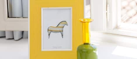 A framed artwork of a striped horse on a white surface next to a green bottle with a yellow cap.
