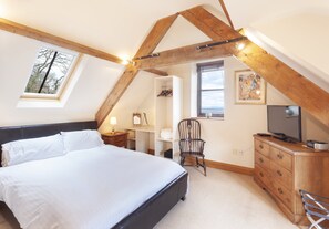 Un dormitorio con cama, una silla, cómoda, televisor y tragaluz.
