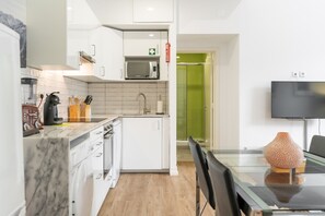 Una cocina moderna con armarios blancos, microondas, cafetera y comedor con mesa y sillas de vidrio.