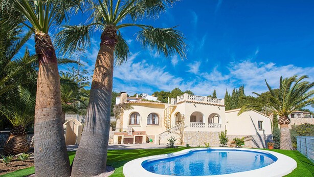 A pool surrounded by palm trees and a Mediterranean-style building with arched windows and a stone facade. - Villa Sabine - PlusHolidays (Benissa)