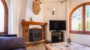 A living room with a fireplace, television, and a chess table. - Villa Sabine - PlusHolidays (Benissa)