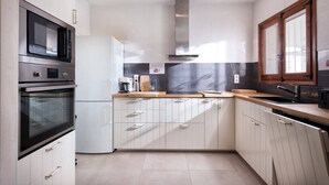 A modern kitchen with white cabinets, stainless steel appliances, and a window with a wooden frame. - Villa Sabine - PlusHolidays (Benissa)