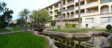 A hotel with multiple balconies, a small bridge over a pond, and palm trees.