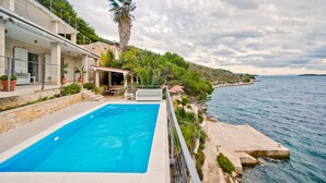 A swimming pool with a view of the sea, a stone building, and a palm tree. - Beachfront Villa Pure Life with Pool (Hvar)