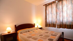 A bedroom with a bed, two bedside lamps, a window with curtains, and a wooden headboard. - APARTMENT PUEBLO AMARRES 2D (L'Escala)