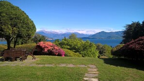 A garden with a bench, a path, and a view of a lake with mountains in the background. - MAJOR LAKE VILLA WITH GARDEN & SWIMMING POOL. AMAZING VIEW ON THE LAKE AND ALPS (Ranco)