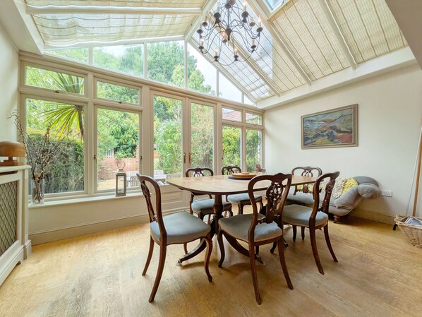 Un espace repas comprenant une grande table, six chaises et une vue sur un jardin grâce à de larges fenêtres.