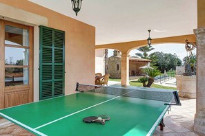 An outdoor ping pong table with a paddle, set against a building with green shutters and a stone wall in the background. - Villa Deu Quarterades (Felanitx)