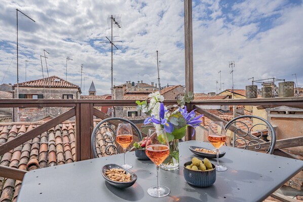 A rooftop terrace with a table set for two, featuring wine glasses, a vase with flowers, and bowls of almonds and pears. - Ca' Grassi 3 Venetian Terrace (Venice)
