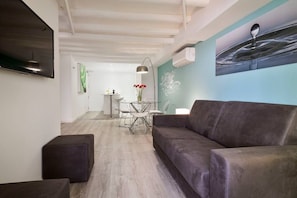 A modern living room with a grey sofa, a dining area with a table and chairs, and a wall-mounted TV.