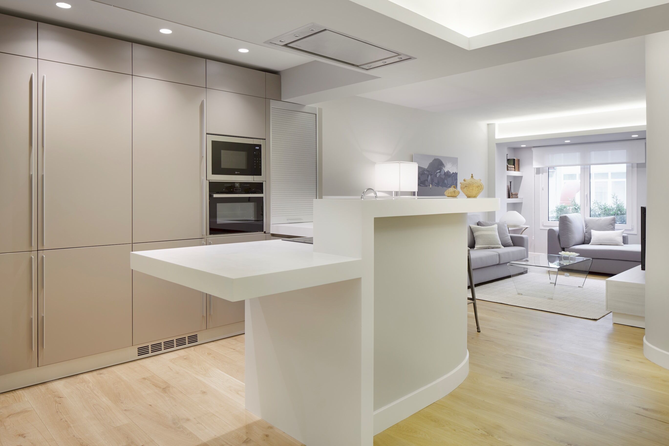 A modern kitchen with built-in appliances, a white countertop, and a dining area with a glass table.
