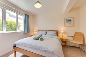 A bedroom with a bed, two bedside tables with lamps, a chair, a window with curtains, and a painting on the wall.