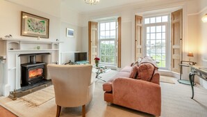 A living room with a fireplace, a sofa, a chair, and a television. - 2 Bed in Mortehoe (oc-mail1) (Mortehoe)