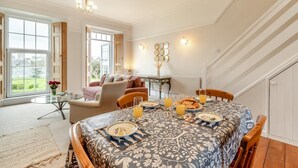 A dining area with a table set for four, a sofa, and a view of the outdoors. - 2 Bed in Mortehoe (oc-mail1) (Mortehoe)