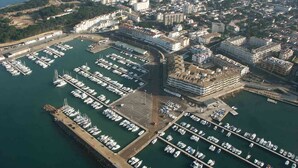 Vue aérienne d’une marina où sont amarrés de nombreux bateaux, entourée d’immeubles résidentiels et, au loin, d’un paysage vallonné.
