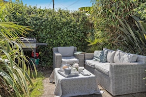 A patio with wicker furniture, a grill, and a table set with a tablecloth and items.