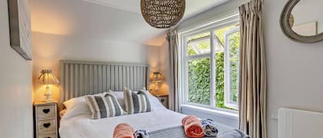 A neatly made bed with striped pillows, a round woven light fixture, and a window with curtains.