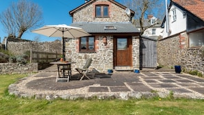 Une maison en pierre avec un patio carrelé, une porte en bois et une antenne parabolique.