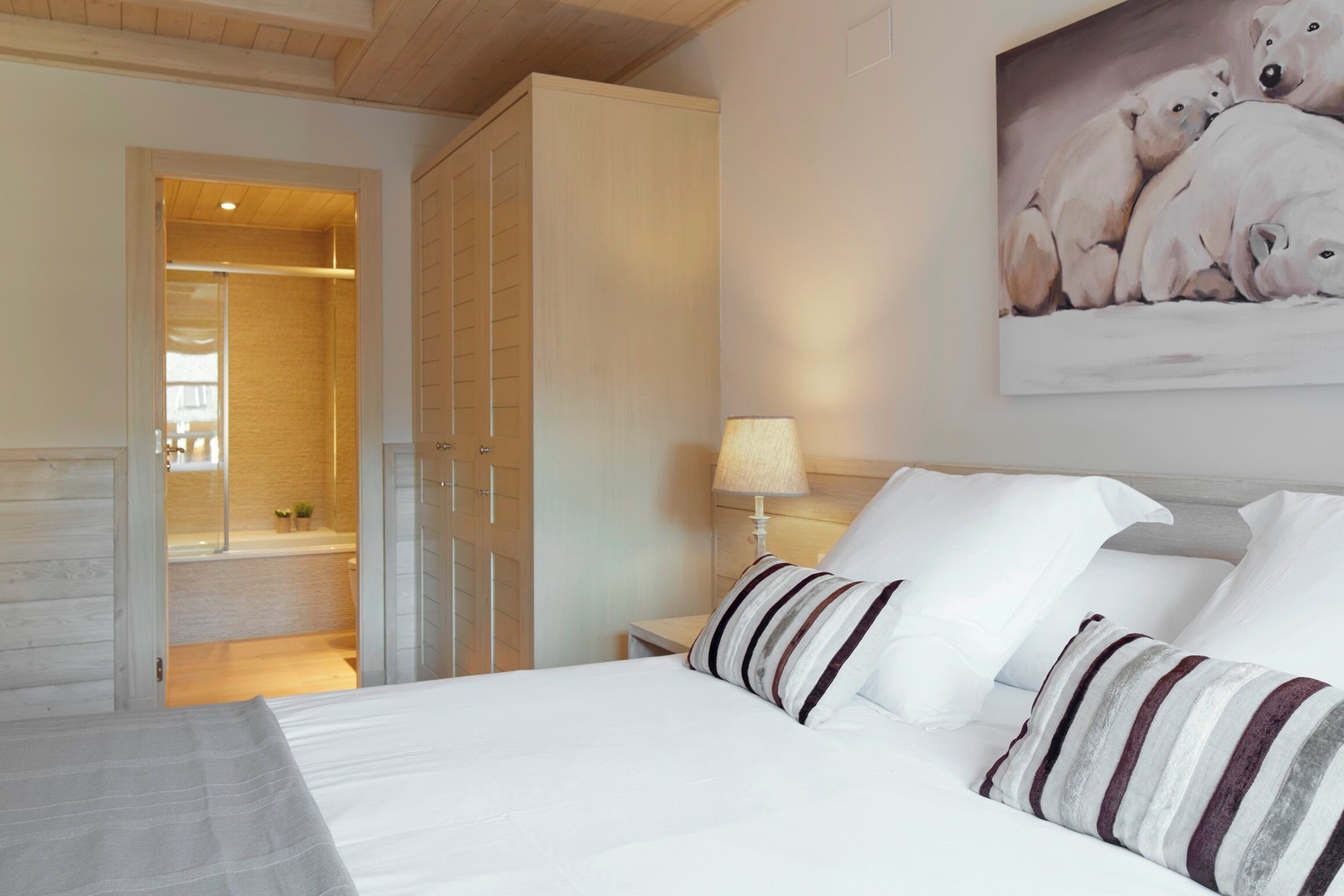 Habitación de hotel con cama, mesita de noche, lámpara, cuadro de osos polares y armario de madera.