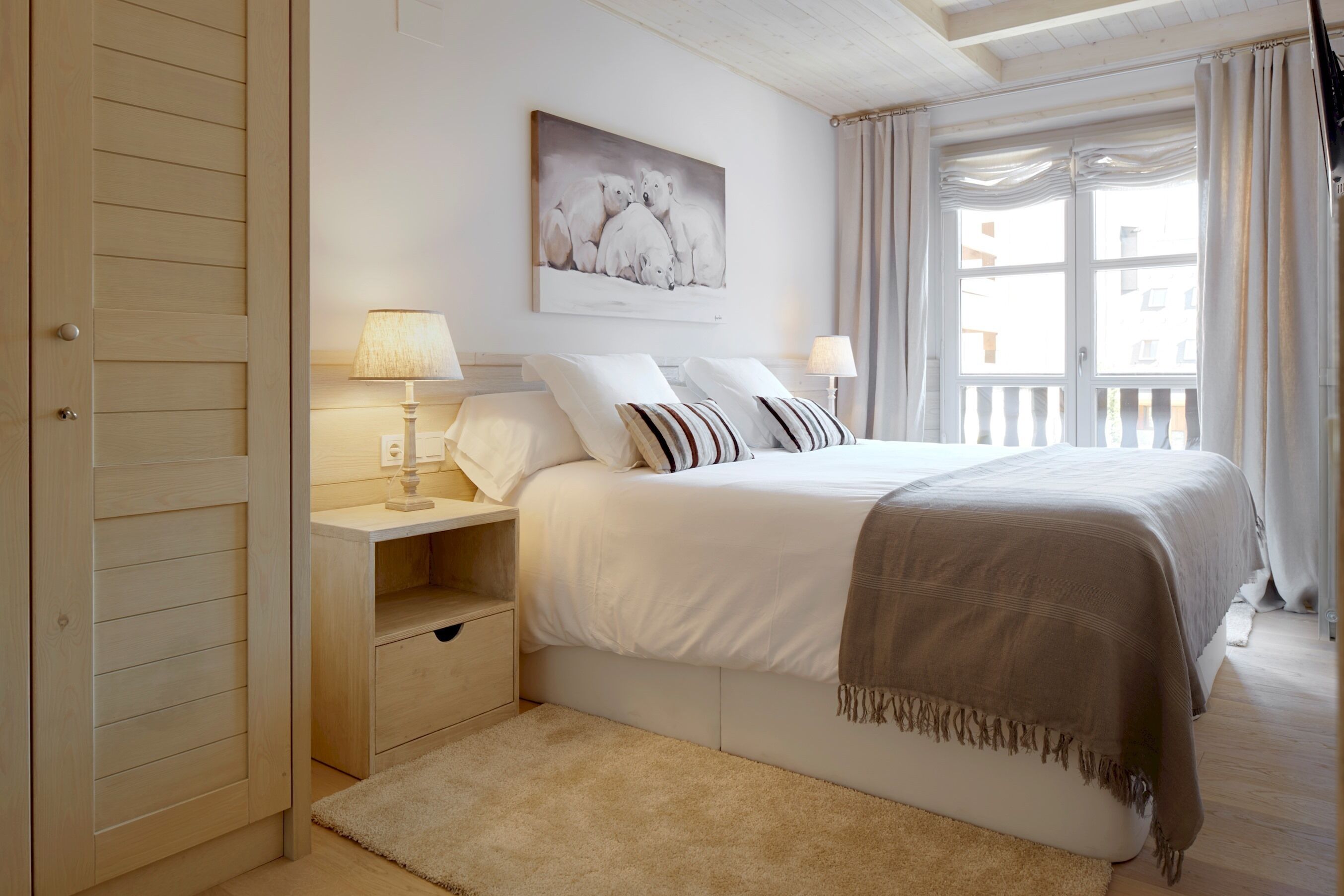 A bedroom with a bed, bedside tables, a nightstand, a window with curtains, and a painting on the wall.