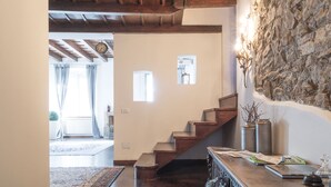 Un escalier en bois menant à un palier, un mur en pierre et une petite table avec des livres et un verre.