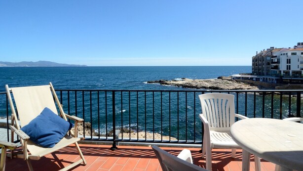 Un balcone con vista sul mare, una sedia, un tavolo e un edificio sullo sfondo.