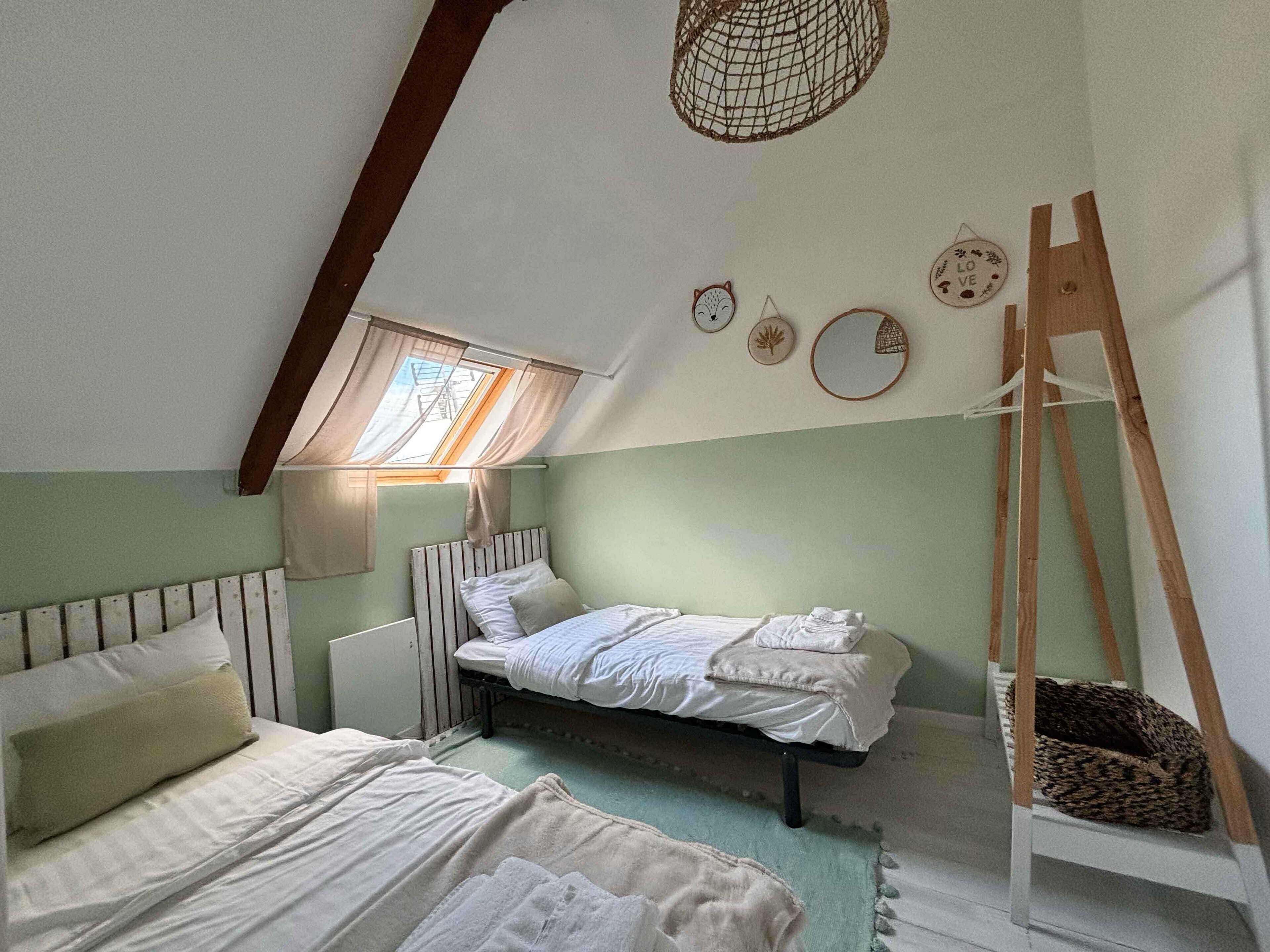 Un dormitorio acogedor en el ático, con techo inclinado, tragaluz, cama, silla y escalera.