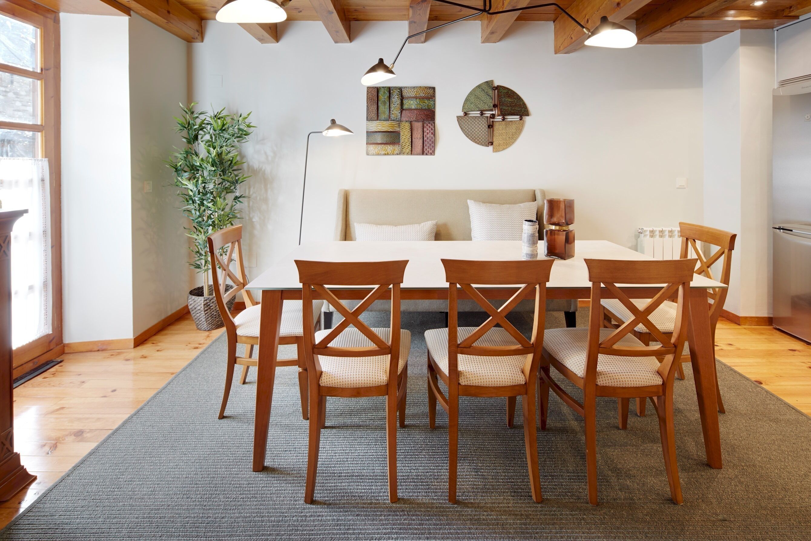 A dining area with a wooden table and chairs, a sofa, and a wall-mounted lamp.