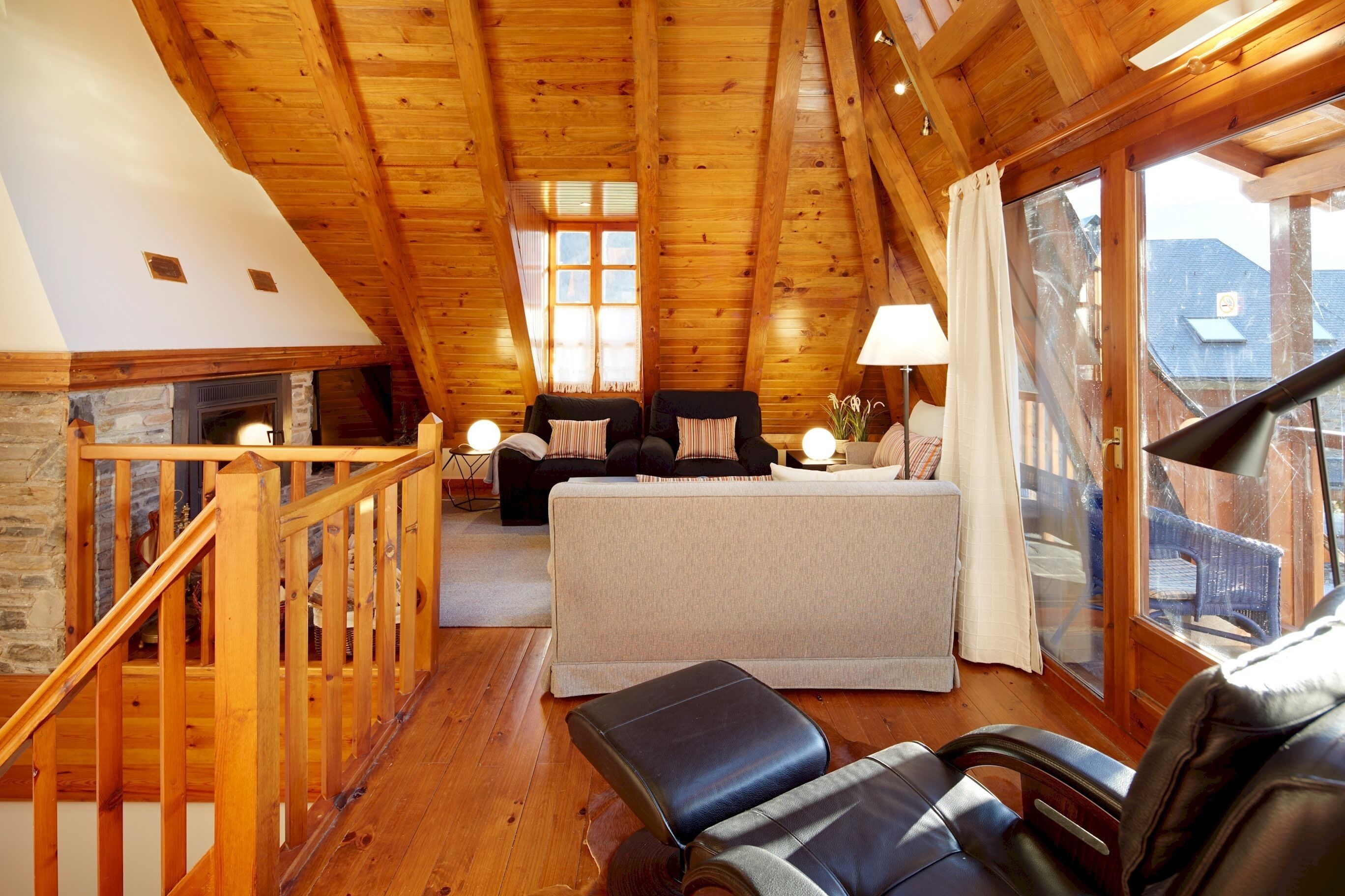 A cozy attic bedroom with a stone fireplace, a bed, a seating area, and large windows offering a view of the outside.