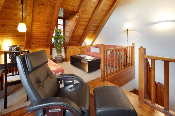 Et hyggeligt loftrum med træloft, sofa, spisebord og trappe.