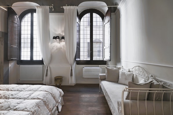 A bedroom with a large bed, a smaller sofa, and a window with curtains.