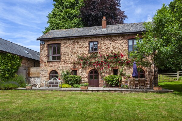 A stone house with a front porch, a wooden fence, and a lawn. - Mill Cottage, Luxborough (Luxborough)