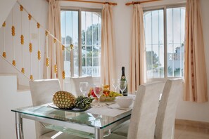 A dining area with a glass table, chairs, a fruit bowl, wine glasses, and a bottle of wine.
