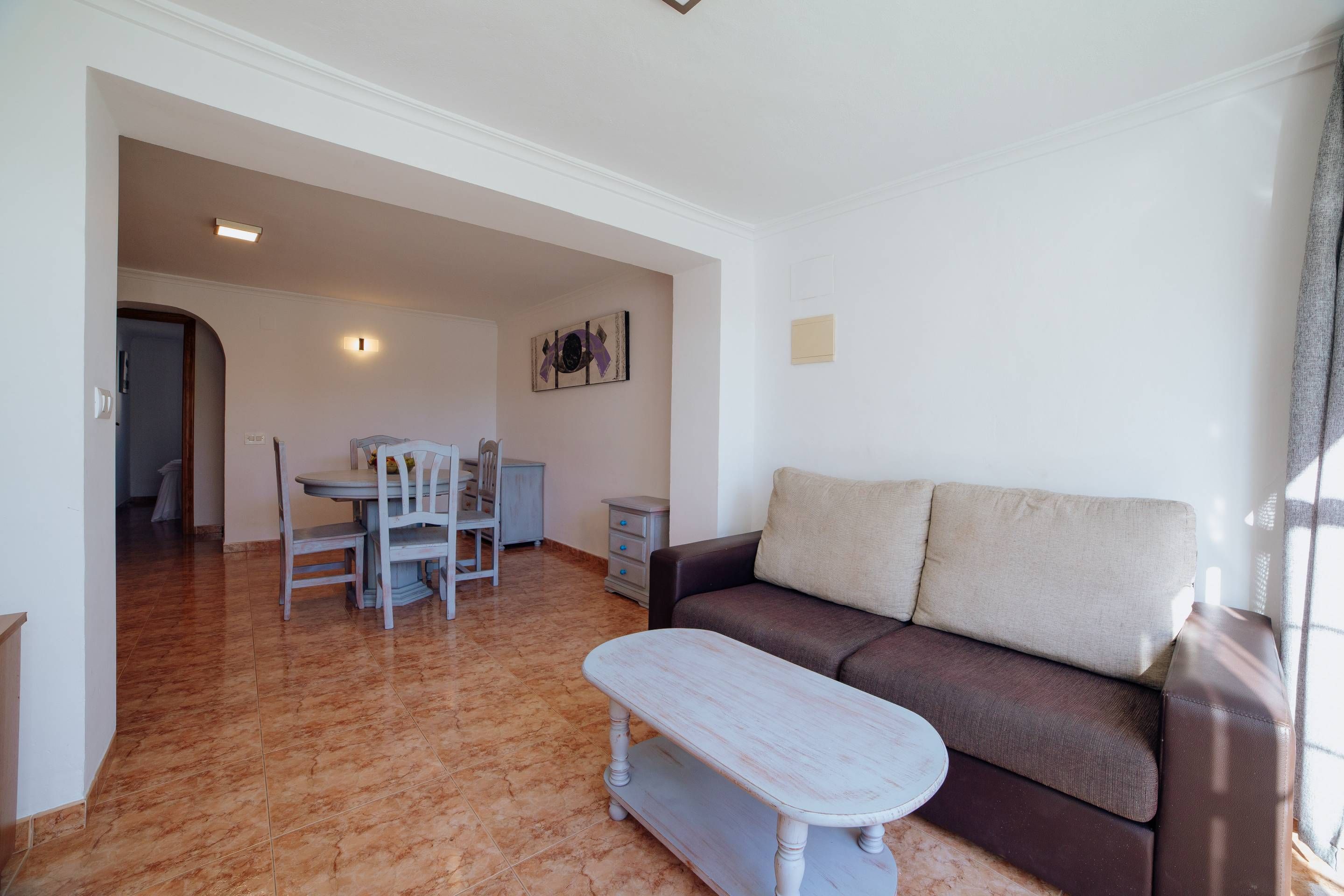 A living room with a brown sofa, a white coffee table, and a dining area with a table and chairs.